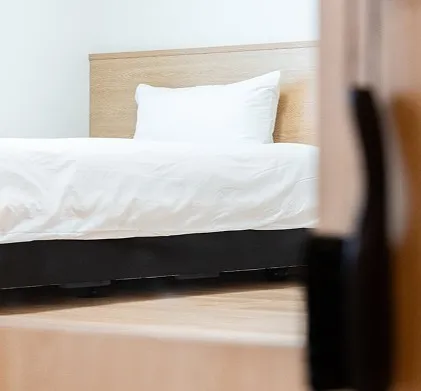 扉の先に見える、清潔で整えられた白いシーツのベッド。