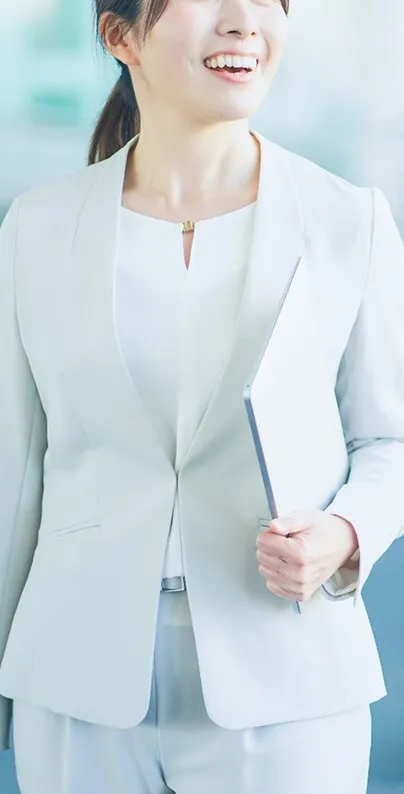 ノートPCを腕に抱え、明るい笑顔を見せるスーツ姿の女性。