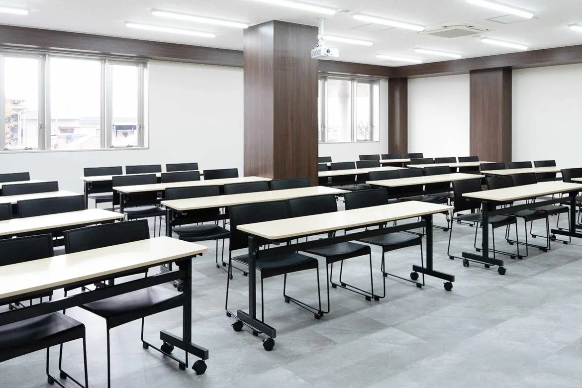 スクール形式にデスクと椅子が整然と並んだ、広々とした会議室。天井にはプロジェクターも完備され、大人数での研修やセミナーに最適な空間。