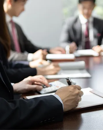 会議室でデスクを囲み、スーツ姿で打ち合わせを行う人々。