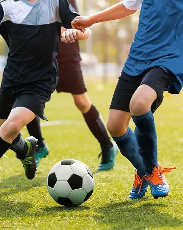 芝生の上でサッカーボールを競り合う選手たちの足元のカット。